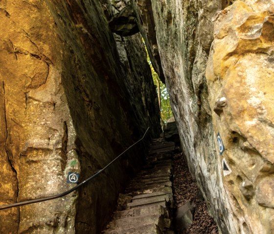 Ein schmaler Pfad mit Steinstufen führt durch eine enge Felsenschlucht. Die Wände sind steil und von natürlichem Licht beleuchtet., © Dominik Ketz