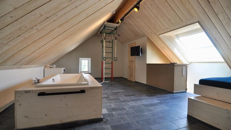 Ein stilvolles Dachzimmer mit hölzernen Wänden und einem modernen Badezimmer. Es gibt eine Badewanne und viel Tageslicht durch die Fenster.