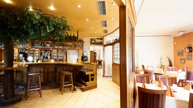 Ein gemütliches Restaurant mit einer Holzbar und vielen Tischen. Die Einrichtung ist warm und einladend, perfekt für ein entspanntes Essen.