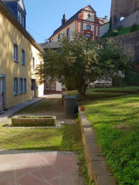 Ein ruhiger Innenhof mit einem grünen Rasen, einem Müllcontainer und einem Blumenbeet. Im Hintergrund ist ein historisches Gebäude sichtbar.