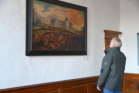 Eine Person betrachtet ein Gemälde an der Wand. Das Bild zeigt eine beeindruckende Landschaft mit historischen Gebäuden.