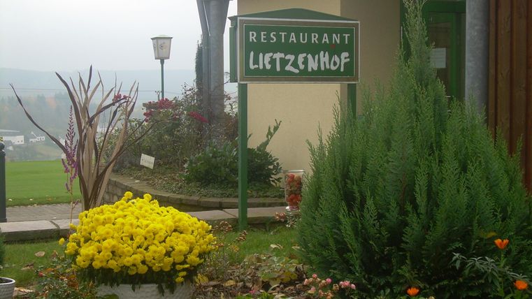 Un restaurant nommé "Lietzenhof" est visible, entouré d'un jardin fleuri. Des fleurs colorées et des plantes décorent l'entrée.