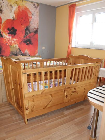 Een gezellig kinderbed van hout staat in een lichte kamer. Aan de muur hangen levendige afbeeldingen en de ramen laten veel daglicht binnen.