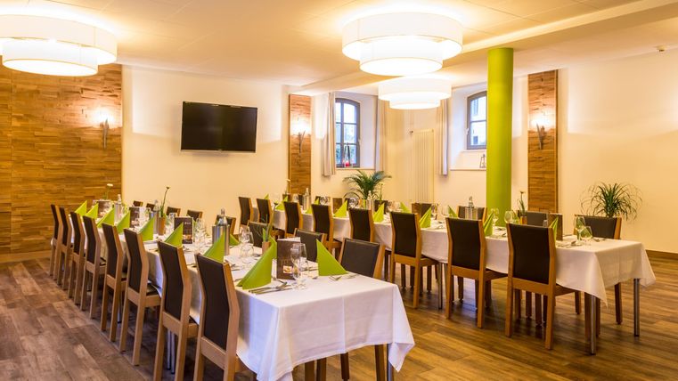 Een stijlvol ingerichte evenementenruimte met lange tafels en stoelen. De tafels zijn gedecoreerd met witte tafellakens en groene servetten.