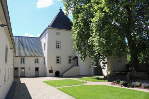 Un bâtiment historique avec un toit pointu et un jardin vert attenant. L'environnement est lumineux et accueillant, avec des arbres et une pelouse bien entretenue.
