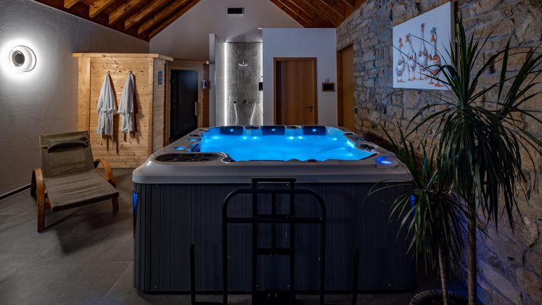 Ein moderner Wellnessbereich mit einem beleuchteten Whirlpool. Im Hintergrund sind eine Sauna und eine entspannende Liege zu sehen.