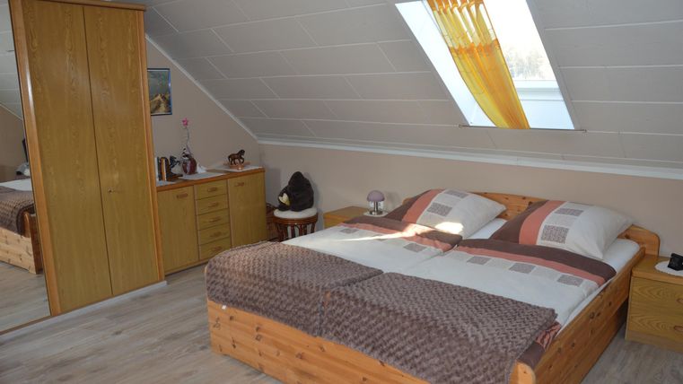 A cozy bedroom with a double bed and bright walls. Large windows and wooden cabinets create an inviting atmosphere.