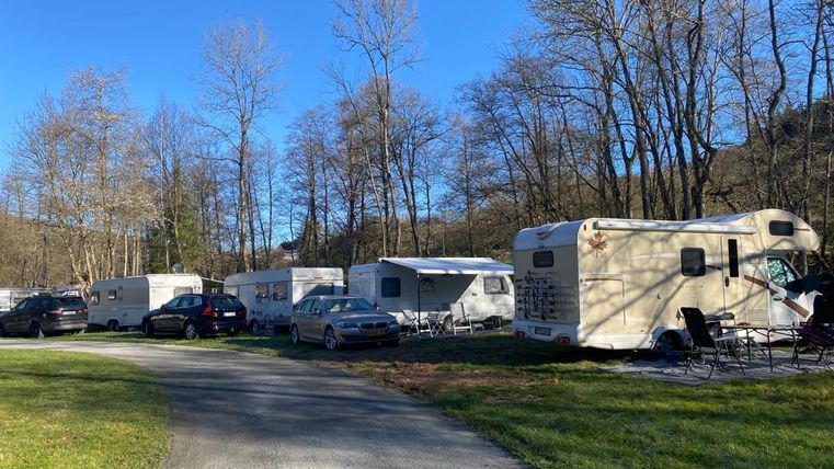 Ein Wohnmobilpark umgeben von Bäumen. Es stehen mehrere Wohnmobile und Autos entlang eines geschwungenen Weges.