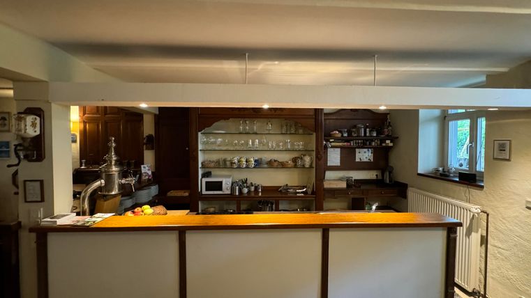 Une cuisine confortable avec un comptoir en bois et des étagères ouvertes. En arrière-plan, on peut voir différents appareils de cuisine et des fenêtres.