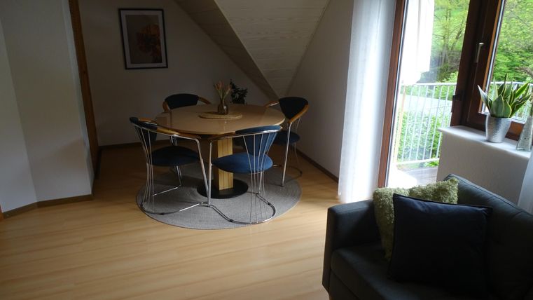 Une pièce claire et moderne avec une table à manger ronde et des chaises bleues. Un canapé confortable et de grandes fenêtres offrent une vue sur l'extérieur.