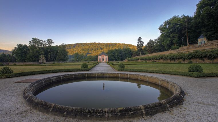Gartenpavillon von Schloss Weilerbach mit Brunnen im Vordergrund und Bäumen im Hintergrund.