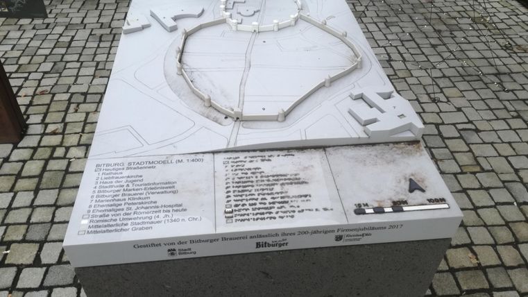 Ein Modell einer historischen Stadtanlage, dargestellt auf einem grauen Sockel. Die Beschriftungen und Details sind gut sichtbar und bieten eine informative Übersicht.