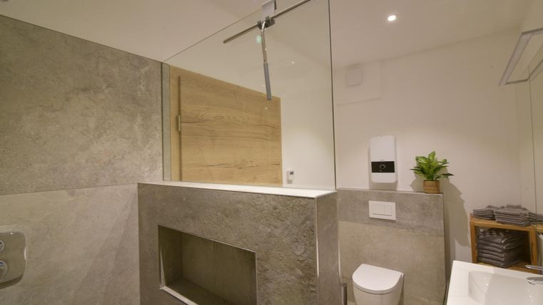 Een moderne badkamer met stenen muren en een open douche. De ruimte is licht en goed uitgerust met houten details en planten.