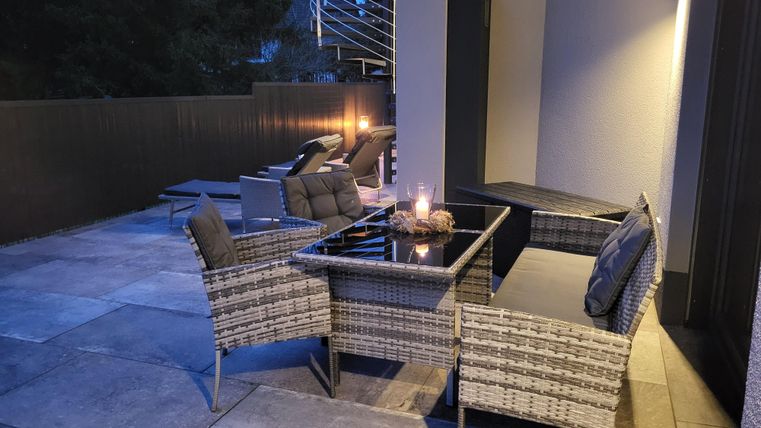 Un espace extérieur confortable avec des meubles modernes et un éclairage tamisé. L'atmosphère est détendue et accueillante.