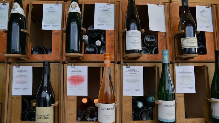 Een gezellige ruimte met een kleine tafel en stoelen. Aan de muur staan planken met wijnflessen en andere drankjes.