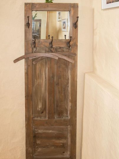 Een rustieke houten kast met een spiegel en meerdere kledinghaken. De muren zijn in een zachte beigeton gehouden.