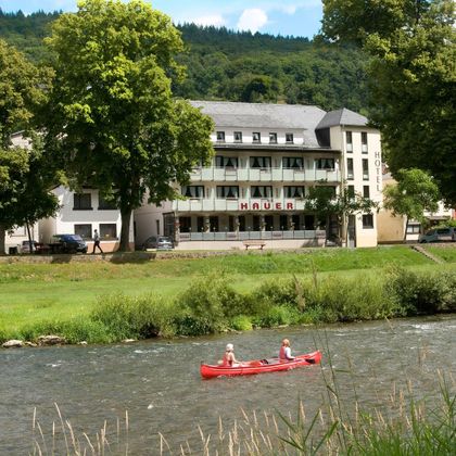Un bel hôtel au bord de la rivière avec des arbres verts et un ciel dégagé. Deux personnes pagaient dans le canoë rouge sur l'eau.