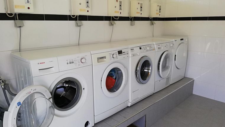 Een reeks witte wasmachines in een lichte ruimte. Aan de muur zijn besturingspanelen geïnstalleerd.