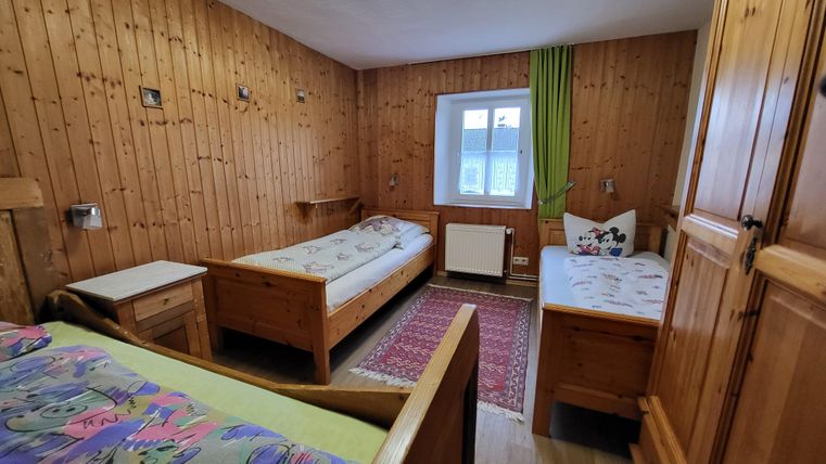 A simple room with wood paneling and two single beds. There is a window with a green curtain and a carpet on the floor.
