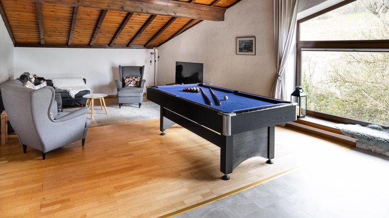 A stylish living room with a pool table and a cozy seating area. Large windows provide plenty of natural light and a view outside.