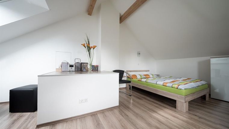 Une chambre moderne avec un lit, un bureau et une chaise. La pièce a des murs clairs et un sol en bois, avec un design cosy et minimaliste.