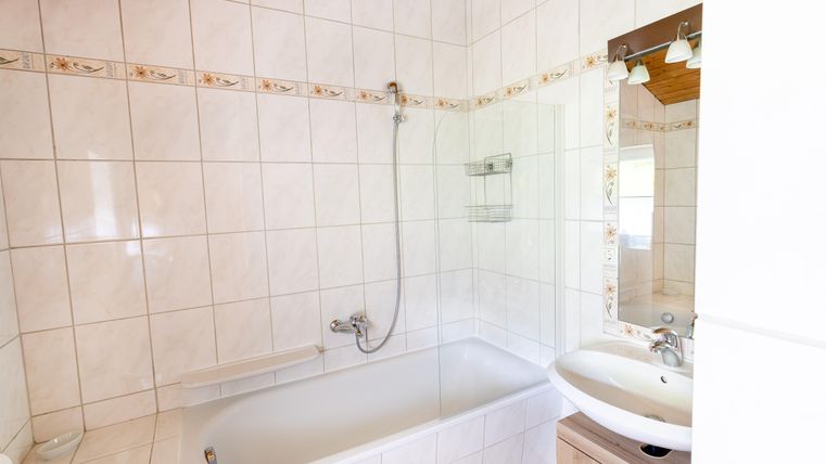A bright bathroom with a bathtub and a shower. The walls are tiled with white tiles and a decorative border.