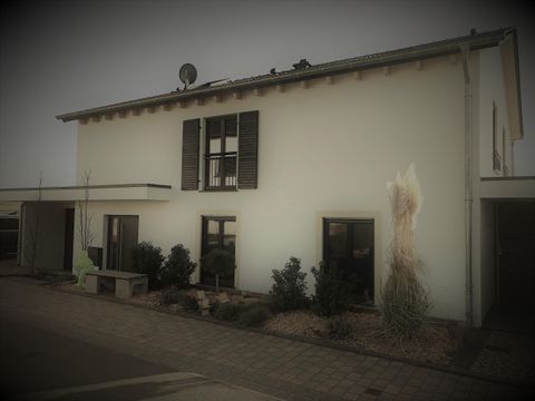 Ein modernes Haus mit weißen Wänden und dunklen Fensterläden. Es gibt Pflanzen im Vordergrund und eine Satellitenschüssel auf dem Dach.