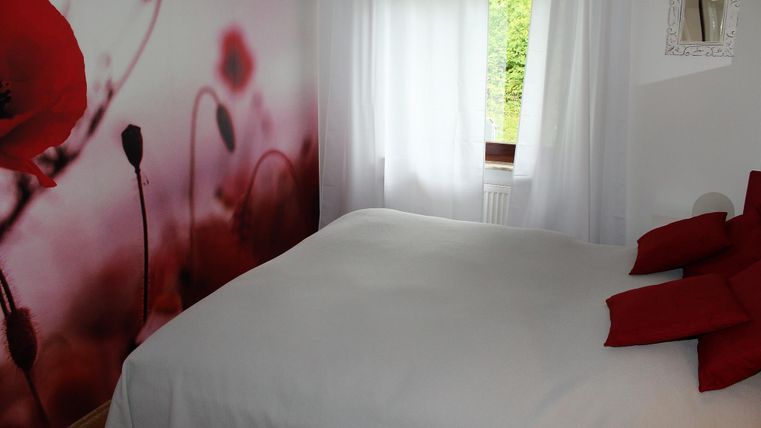 Ein gemütliches Schlafzimmer mit einem großen Bett und roten Kissen. An der Wand ist ein dekoratives Motiv von roten Mohnblumen zu sehen.