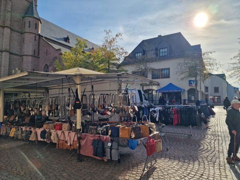 Ein lebhafter Marktstand mit bunten Taschen und handgemachten Textilien. Die Stände sind unter roten Zelten aufgestellt und bieten eine Vielzahl von Produkten an.