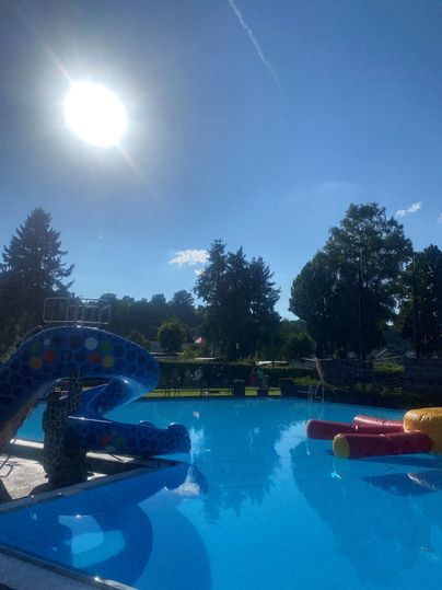 Een zwembad met een glijbaan en kleurrijke waterattracties. De lucht is helder en de zon schijnt fel.