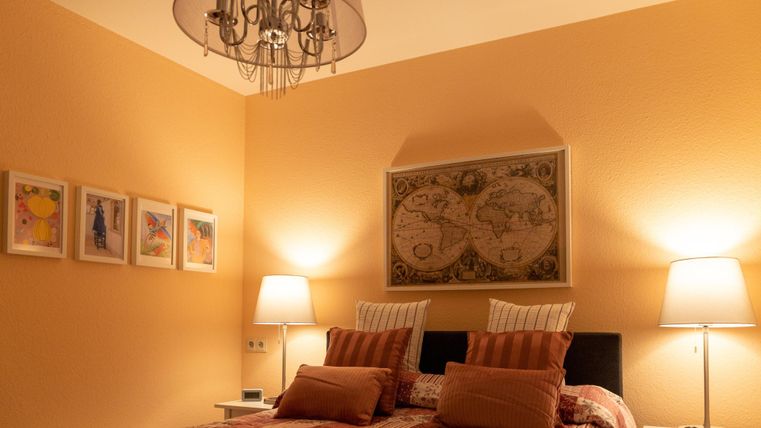 Ein gemütliches Schlafzimmer mit einem Doppelbett und warmen Farben. An den Wänden hängen Bilder und eine Weltkarte, während sanfte Lampen für eine angenehme Beleuchtung sorgen.