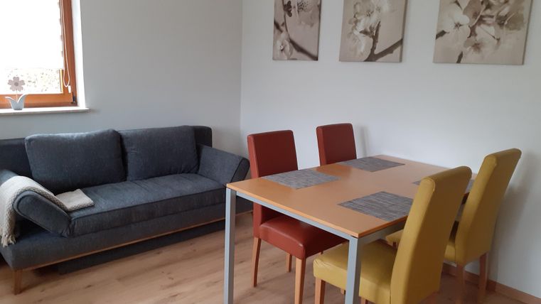 Un espace de vie confortable avec un canapé bleu et une table à manger lumineuse. Autour de la table, il y a des chaises orange et jaunes.