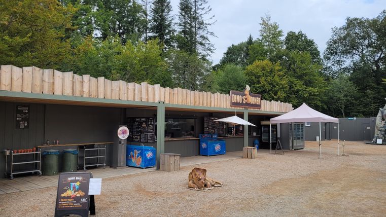 Ein Imbissstand inmitten von Bäumen. Der Bereich ist sauber und hat Tische und Bänke für Gäste.