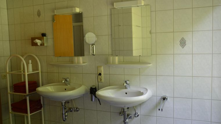 A modern bathroom with two sinks and large mirrors. In the background, towels and a shelf are visible.
