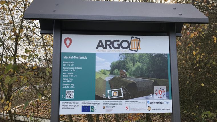 Ein Infostand mit dem Titel "ARGO IV" und Informationen zu einer Sehenswürdigkeit. Im Hintergrund sind Bäume und der Himmel sichtbar.