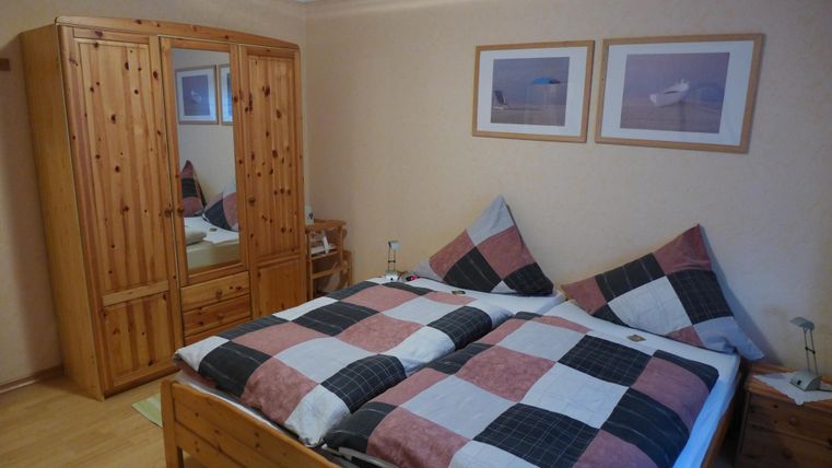 Ein gemütliches Schlafzimmer mit einem Doppelbett und karierten Bettdecken. An der Wand hängen zwei Bilder und es gibt einen Holzschrank mit Spiegel.
