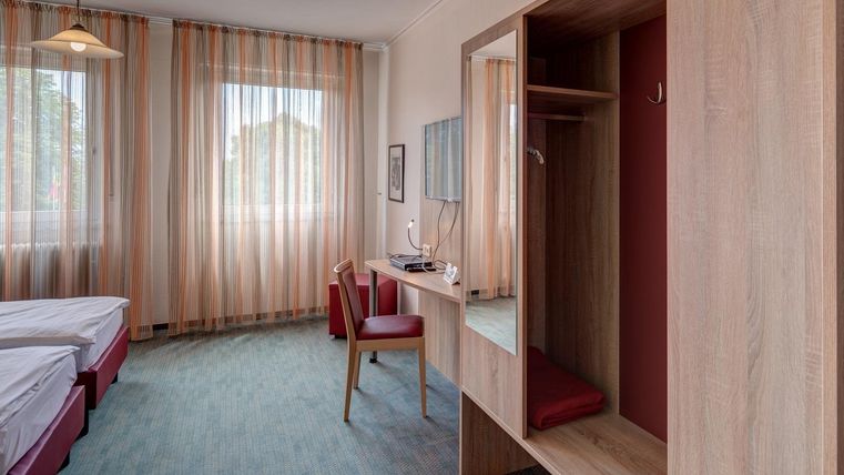 Une chambre d'hôtel moderne avec deux lits, un bureau et une grande fenêtre. Les murs sont décorés de rideaux à rayures et il y a une armoire.
