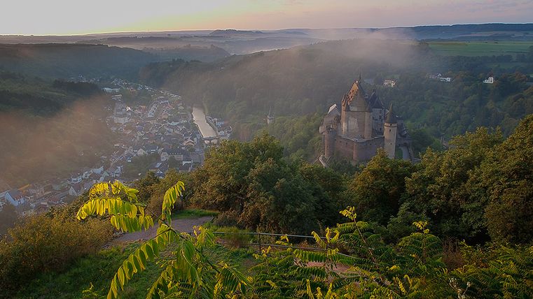 Blick auf das Tal von Vianden mit Schloss und Fluss, umgeben von grünen Hügeln.