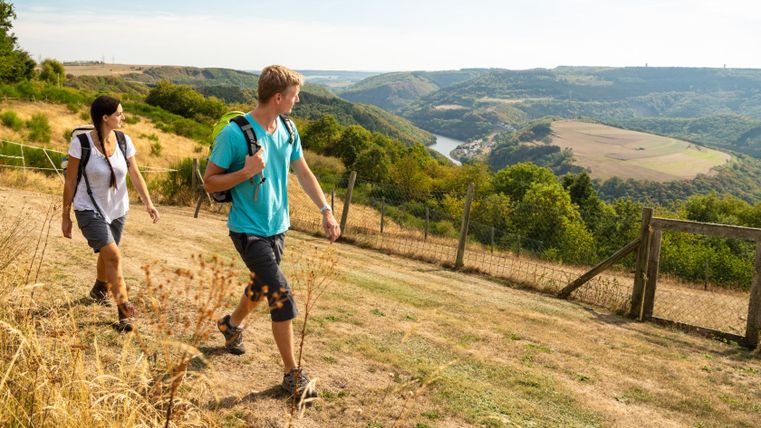Zwei Wanderer auf einem Hügel mit Blick auf eine Flusslandschaft.