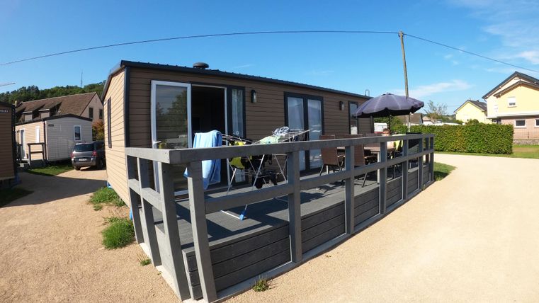 Une maison de vacances moderne avec une terrasse et des meubles de jardin. L'environnement est calme et verdoyant, idéal pour des journées relaxantes.