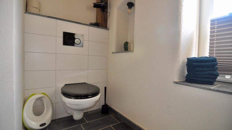 Ein modernes Badezimmer mit einer Toilette und grauen Fliesen. Handtücher sind ordentlich gestapelt und es gibt eine kleine Fensternische.