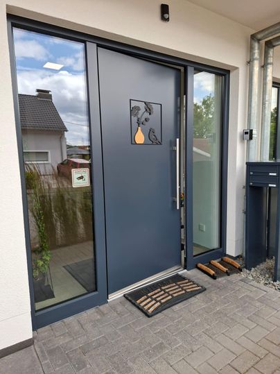 A modern front door with a decorative motif and a doormat. The entrance is clean and well-lit.