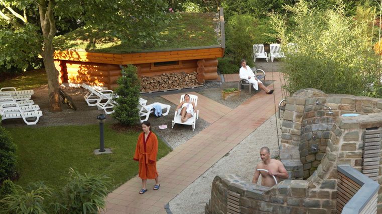 Een ontspannend spagebied met een sauna en ligstoelen. Enkele personen genieten van de rust in de natuur.