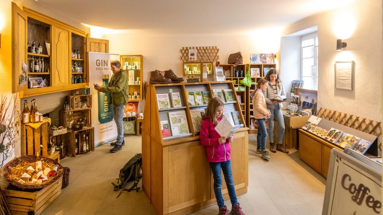 Een gezellige verkoopruimte met houten meubels en planken vol producten. Mensen kijken rond en een kleine groep doet inkopen.