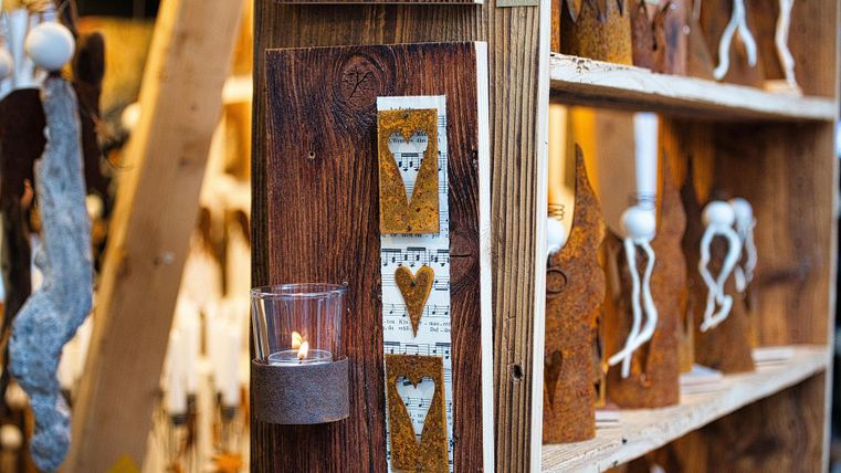 Ein Holzregal mit handgefertigten Dekorationsgegenständen und Kerzen. An der Wand hängen rustikale Elemente mit Herzmotiven.