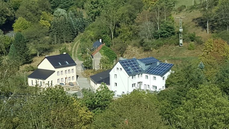 Zwei moderne Häuser in einer grünen Landschaft mit Bäumen. Das größere Haus hat Solarpanele auf dem Dach.
