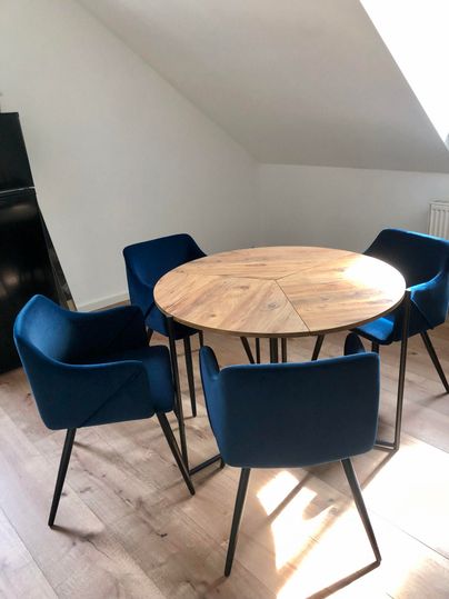 A round wooden table with four blue chairs. The room is brightly and pleasantly furnished.