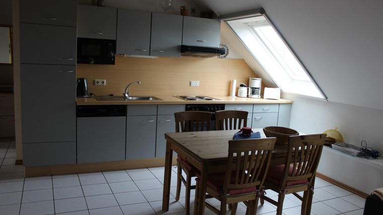 Een moderne keuken met grijze kasten en een eetgedeelte van hout. De kamer heeft een venster dat veel licht binnenlaat.