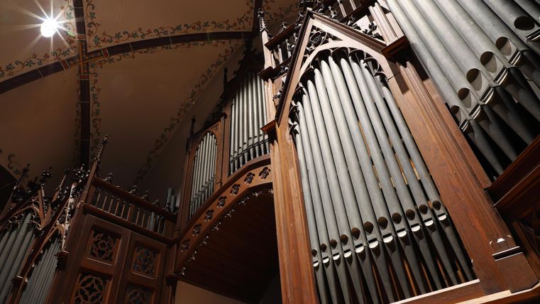 Eine prächtige Kirchenorgel aus Holz mit vielen Pfeifen. Der Blick von unten zeigt die kunstvolle Bauweise und die Details des Instruments.
