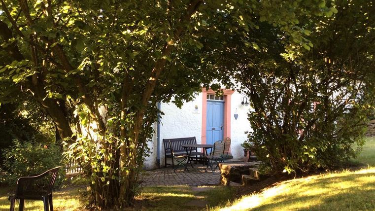 Un joli jardin avec un coin salon confortable et beaucoup de verdure. À l'arrière-plan, on peut voir une maison avec une porte bleue.